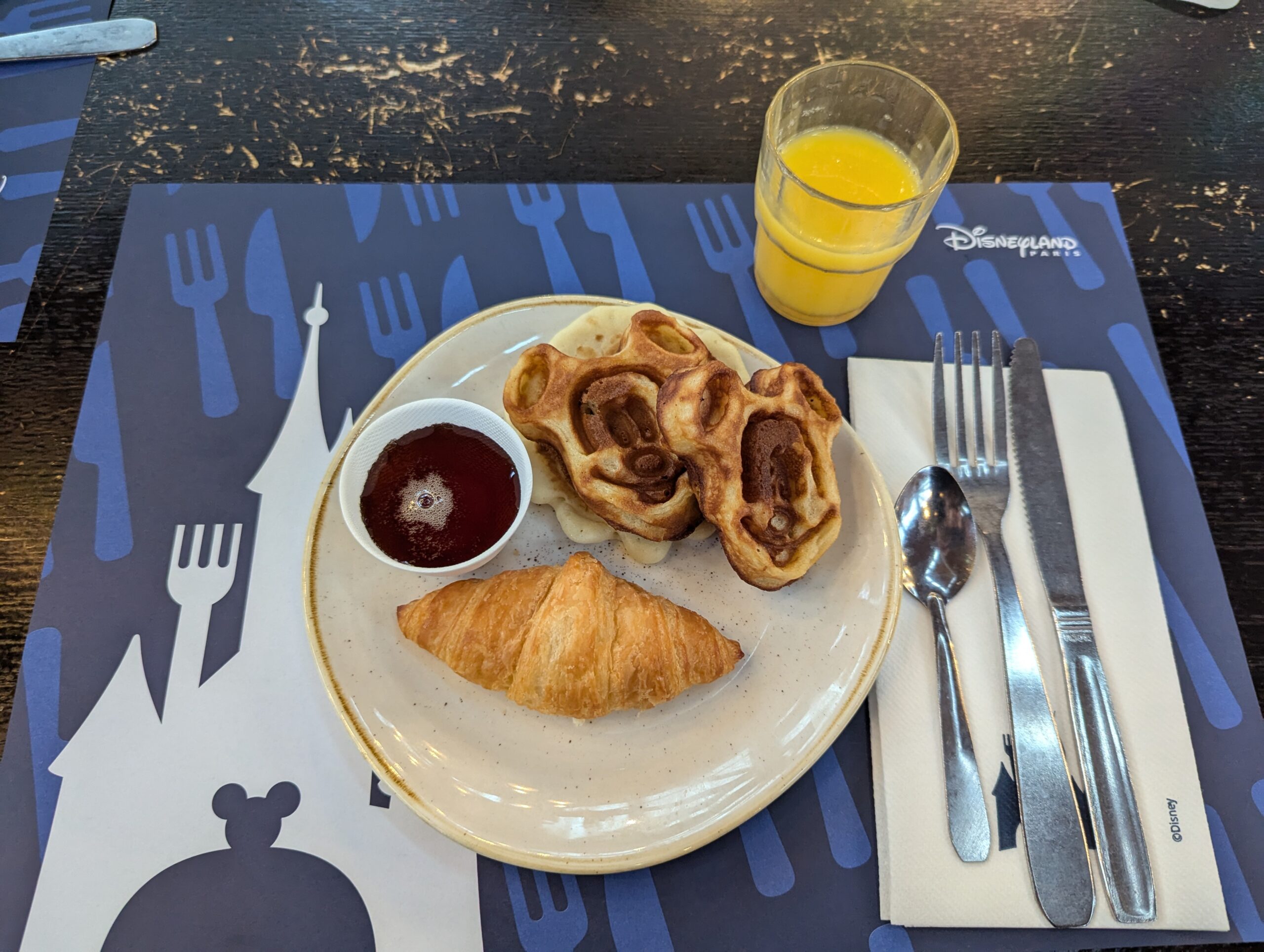 Breakfast of a crescant, waffles, and orange juice.