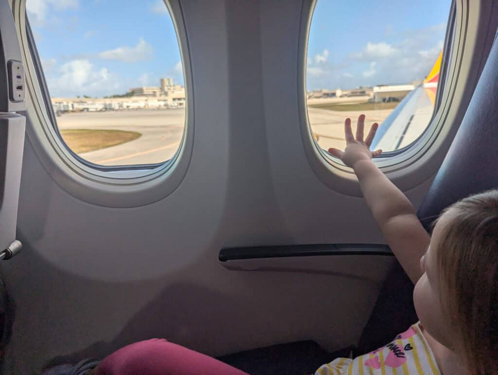 My toddler sittingi n the window seat of the airplane reaching to touch the window
