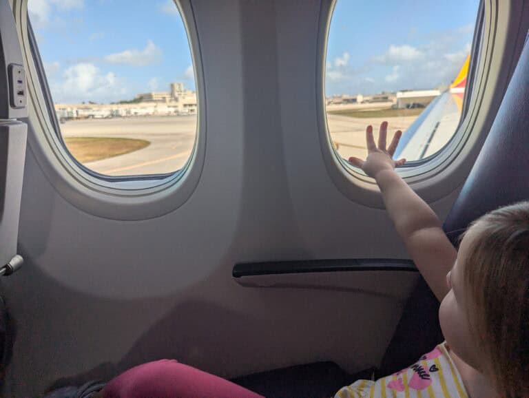 My toddler sittingi n the window seat of the airplane reaching to touch the window