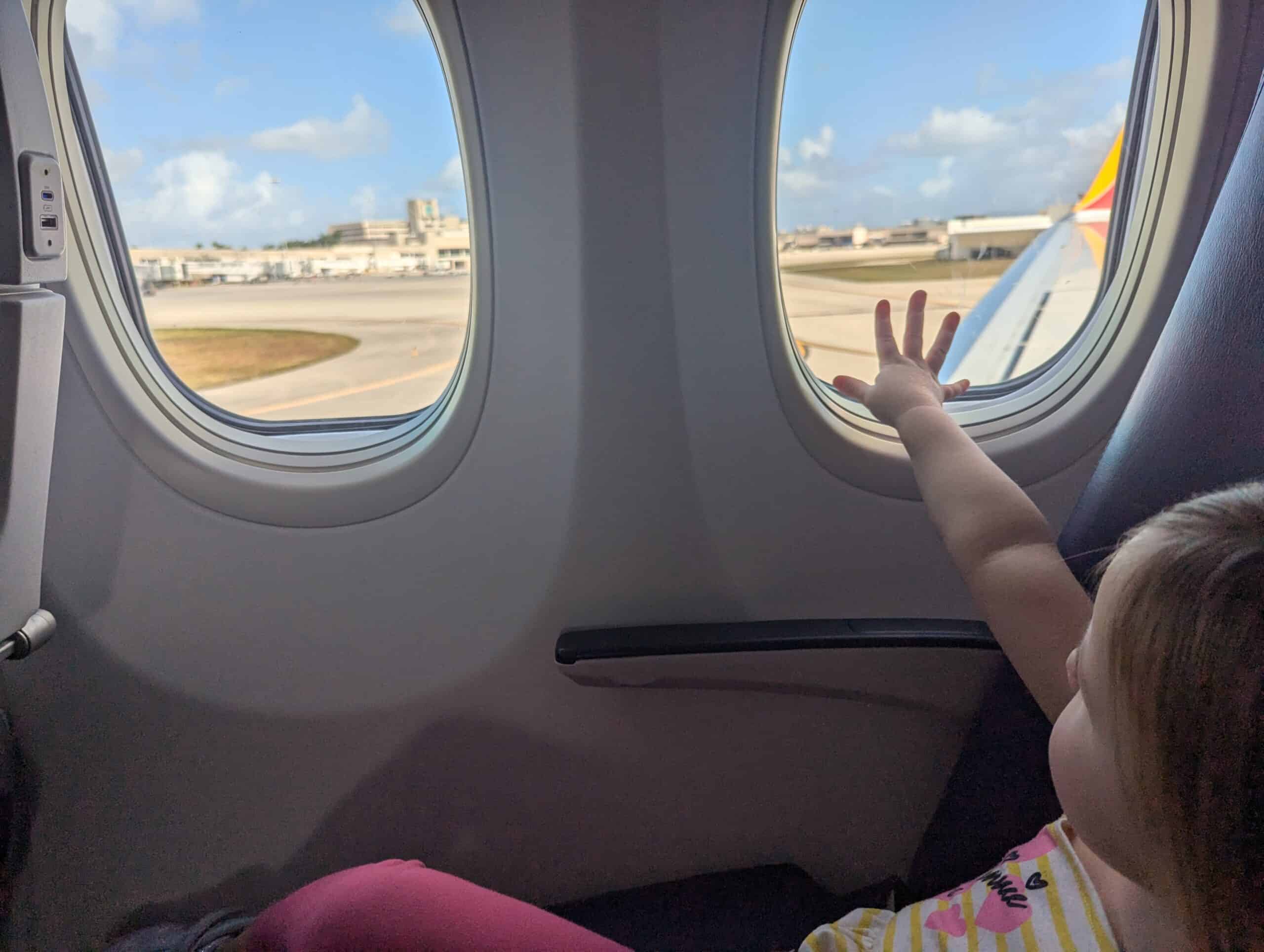My toddler sittingi n the window seat of the airplane reaching to touch the window